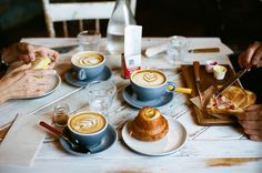 three people sitting at a table with cups of coffee and pastries