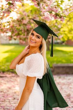 a woman wearing a graduation cap and gown posing for a photo in front of flowers