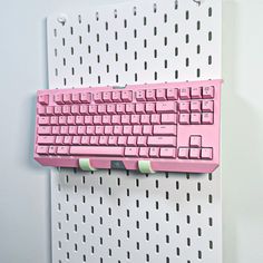 a pink keyboard mounted to the side of a white wall with perfored holes