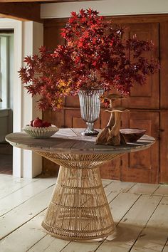 a table topped with a vase filled with red flowers next to a bowl of fruit