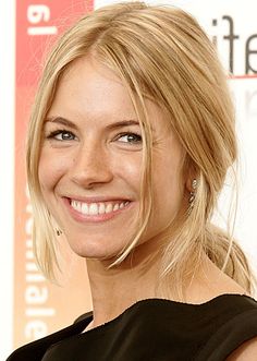 a woman with blonde hair smiling and wearing a black dress on the red carpet at an event