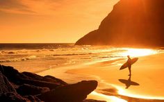 a person holding a surfboard on top of a beach near the ocean at sunset