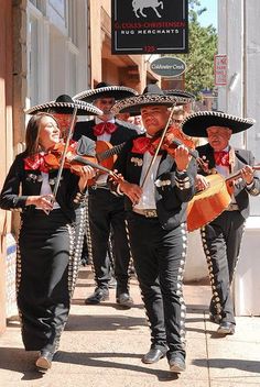 some people are walking down the street with sombreros on their heads and guitars in their hands