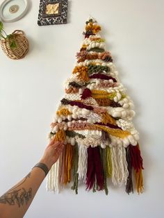 a handmade christmas tree hanging on the wall with tassels and yarn around it