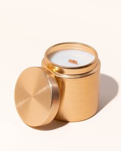 a small gold tin candle with a lid on a white background, next to a smaller one