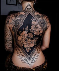 the back of a woman's body with tattoos and flowers on her upper half