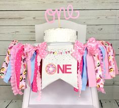 a one year old birthday cake topper on a chair with pink and blue streamers