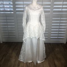 a white wedding dress on display in front of shutters with wood flooring and wooden floors