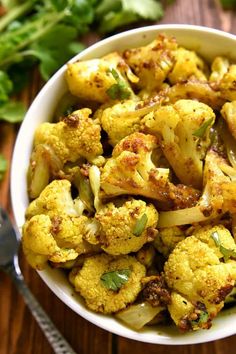 a white bowl filled with cooked cauliflower on top of a wooden table