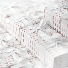 many wrapped presents are stacked on top of each other with white ribbons and bows around them