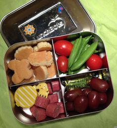 a metal container filled with food on top of a green table covered in fruit and veggies