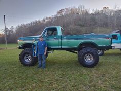 a man standing next to a green truck on top of a lush green field with trees in the background