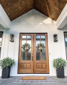 two potted plants sit on the front porch of a house with double doors and windows