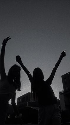 two girls are standing in the dark with their arms up