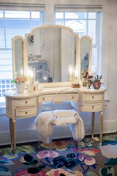 a white vanity with a mirror and stool in front of it on top of a rug