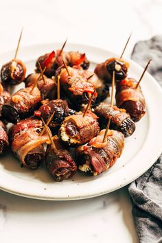 a white plate topped with meat wrapped in toothpicks and bacon on skewers