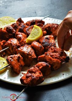 someone is cutting up some meat on a plate with lemons and skewers