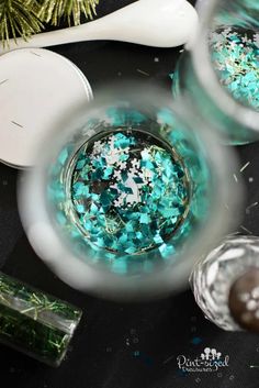 two glasses filled with blue and green confetti on top of a black table