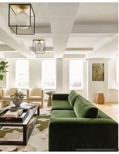 a living room filled with green couches next to two tables and lamps hanging from the ceiling