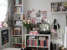 a room filled with lots of books and flowers on top of a white book shelf