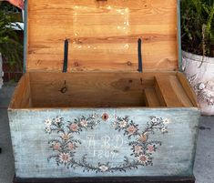 an old trunk with floral designs painted on the outside and inside, sitting in front of some potted plants