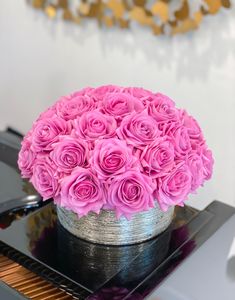 pink roses in a silver vase on top of a piano