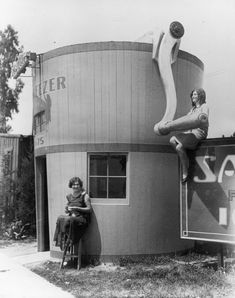 two women sitting on the side of a building with an upside down sign in front of them