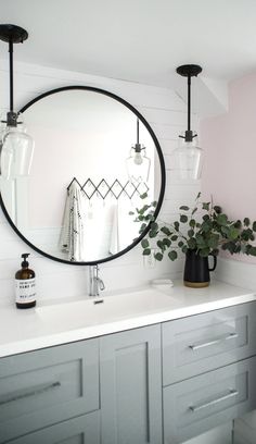 a bathroom with a large round mirror on the wall and two vases filled with plants