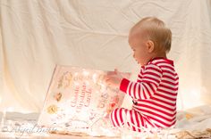 a baby is sitting on the floor reading a book with lights in front of it