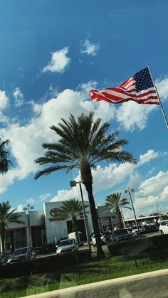 an american flag flying in front of a car dealership with palm trees and cars