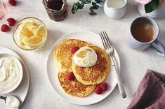 pancakes with whipped cream and raspberries on a white plate next to cups of coffee