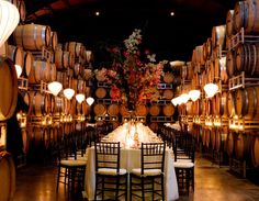 the table is set up in front of many wine barrels with candles and flowers on them