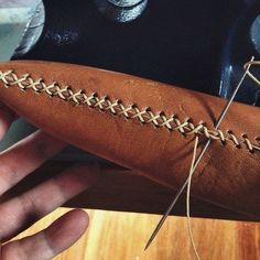 a person holding a brown leather object in their right hand, with some thread on it