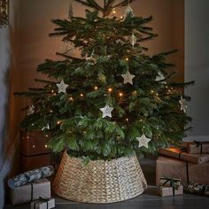 a small christmas tree in a wicker basket with lights on it and presents under the tree