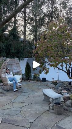 a woman sitting in a chair next to a bird cage on a stone patio area