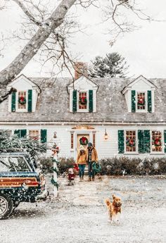 two people and a dog walking in front of a white house with green shutters