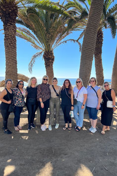 a group of women standing next to each other near palm trees and the ocean in the background