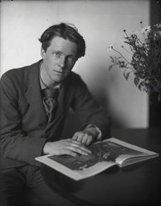 black and white photograph of a man in suit sitting down reading a book with his hand on the cover