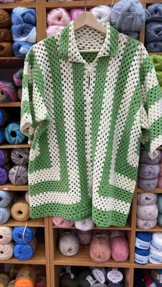 a green and white knitted sweater hanging on a rack in front of skeins of yarn