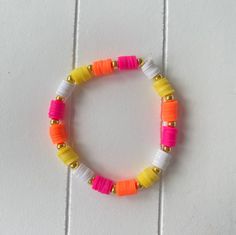 a bracelet made out of plastic beads on a white tile background with gold and pink accents