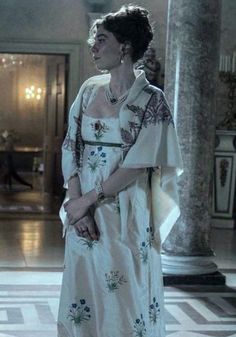 an older woman in a white dress standing in a room with columns and chandeliers