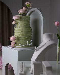 there is a green cake with flowers on the table next to it and a white vase