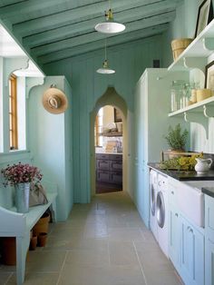 a long narrow kitchen with blue walls and white cabinets, along with a washer and dryer