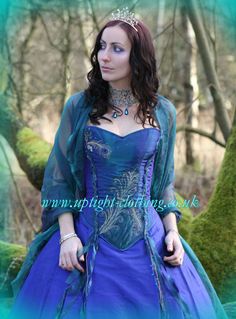 a woman wearing a blue dress and tiara in the woods with mossy trees