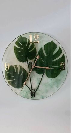 a glass clock with green leaves on the face and numbers is shown in front of a white background