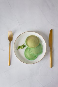 a white plate topped with green plates next to gold forks