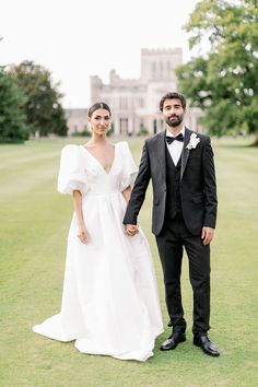 a bride and groom holding hands in front of a large building on the grass field