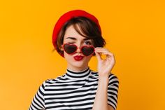 a woman with heart shaped sunglasses on her face and wearing a red hat, striped shirt and black pants