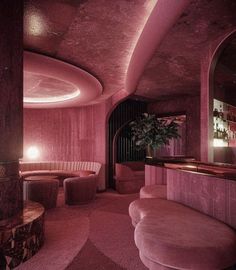 the interior of a bar with pink walls and circular seating area, along with round wooden stools