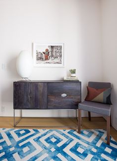 a living room with a blue rug and a chair in front of a painting on the wall